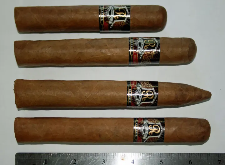 Four cigars from one line laid out above a ruler, with different lengths and thicknesses, one with a pointed head.